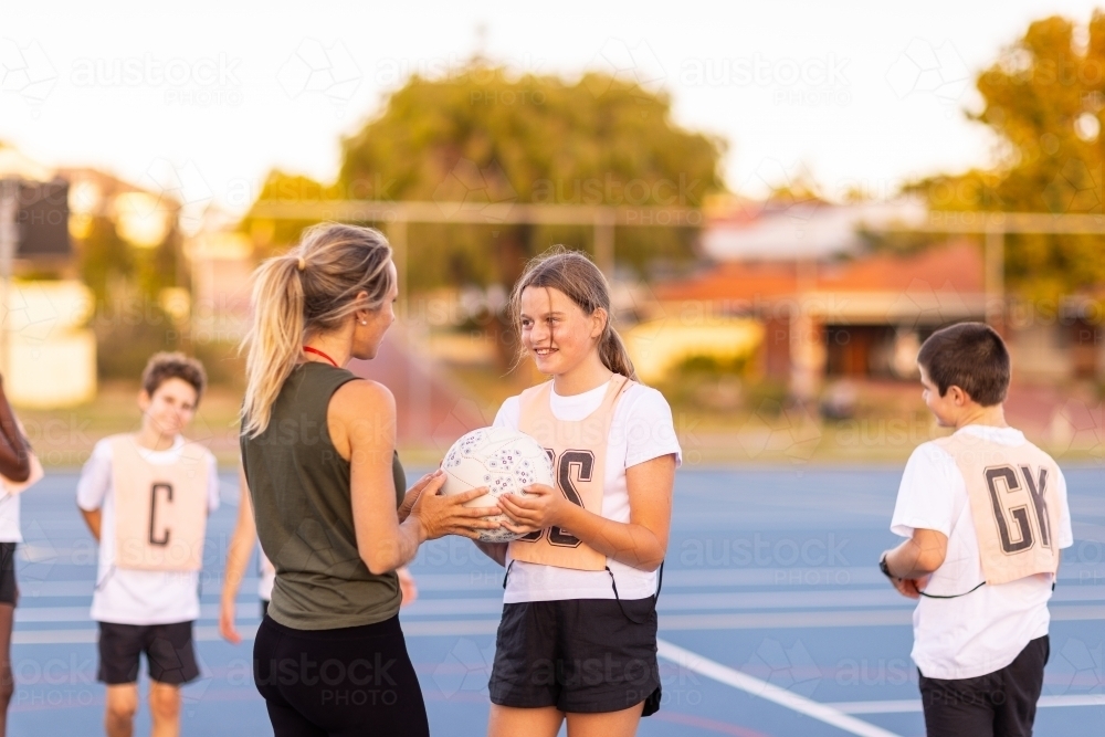 Image of netball coach interacting with girl holding ball at netball ...
