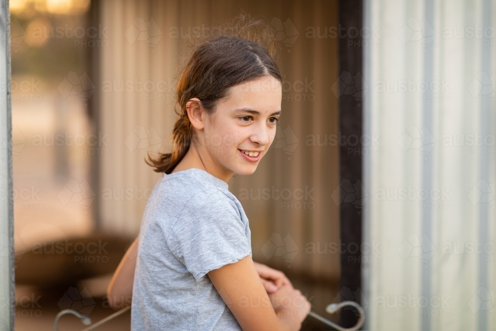 neutral colour photo of girl by herself at shed gate - Australian Stock Image