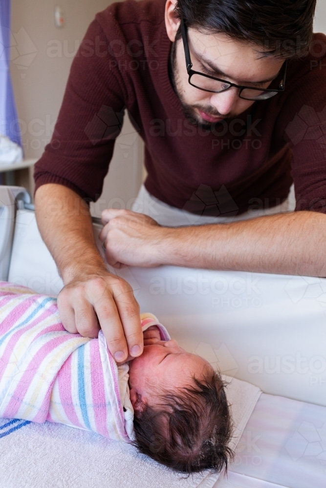 New dad leaning over newborn baby in hospital crib - Australian Stock Image