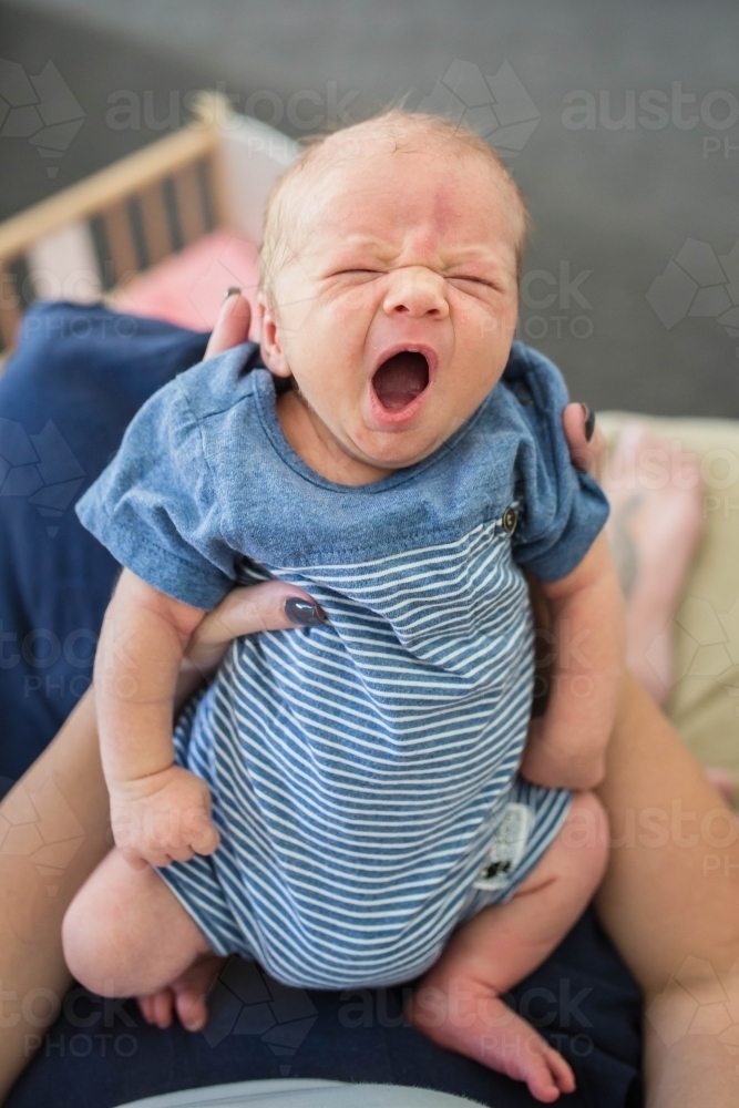 Newborn baby boy lying in mother's arms yawning - Australian Stock Image