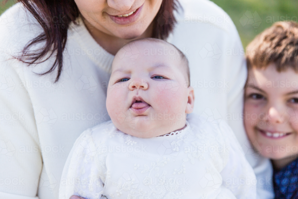 Newborn baby girl poking tongue out while mum and brother smile - Australian Stock Image