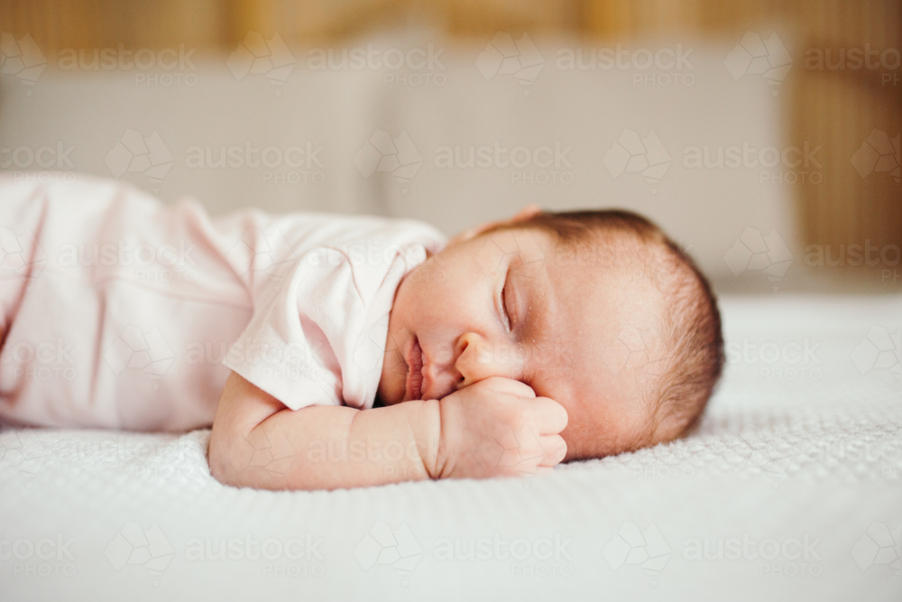 Newborn baby sleeping on her tummy on the bed. - Australian Stock Image