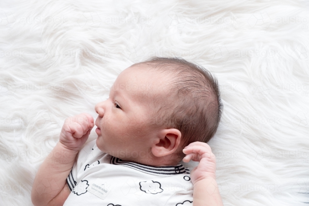 Newborn lying on white fur rug looking away from camera - Australian Stock Image