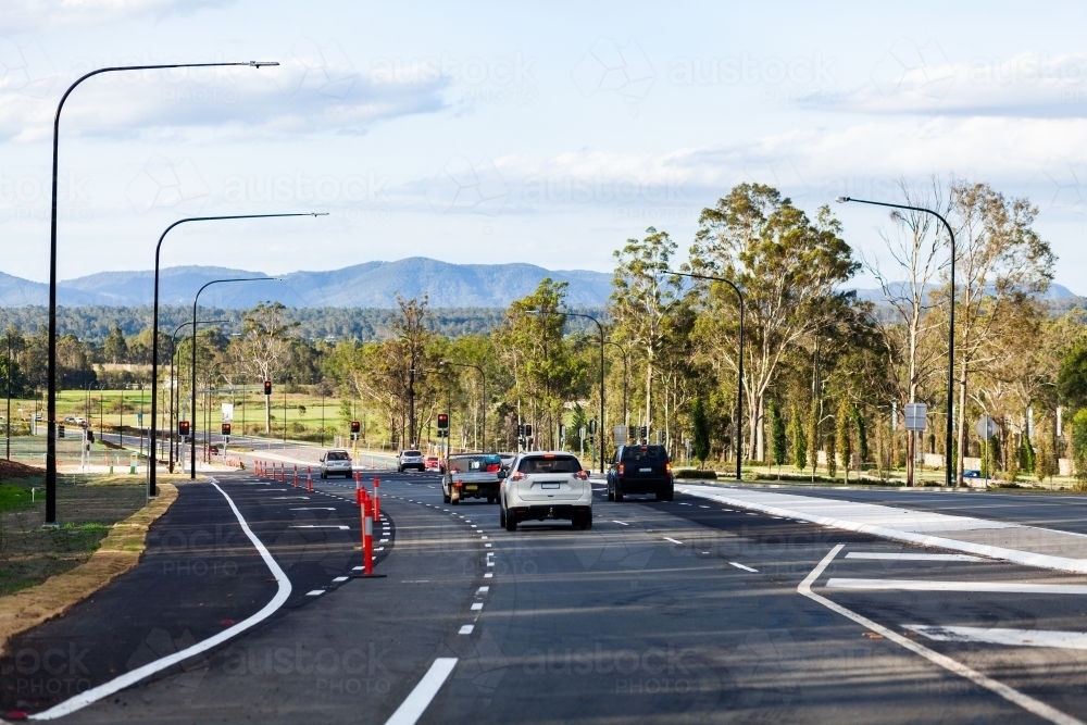 Newly built road infrastructure with cars driving on it towards traffic lights - Australian Stock Image