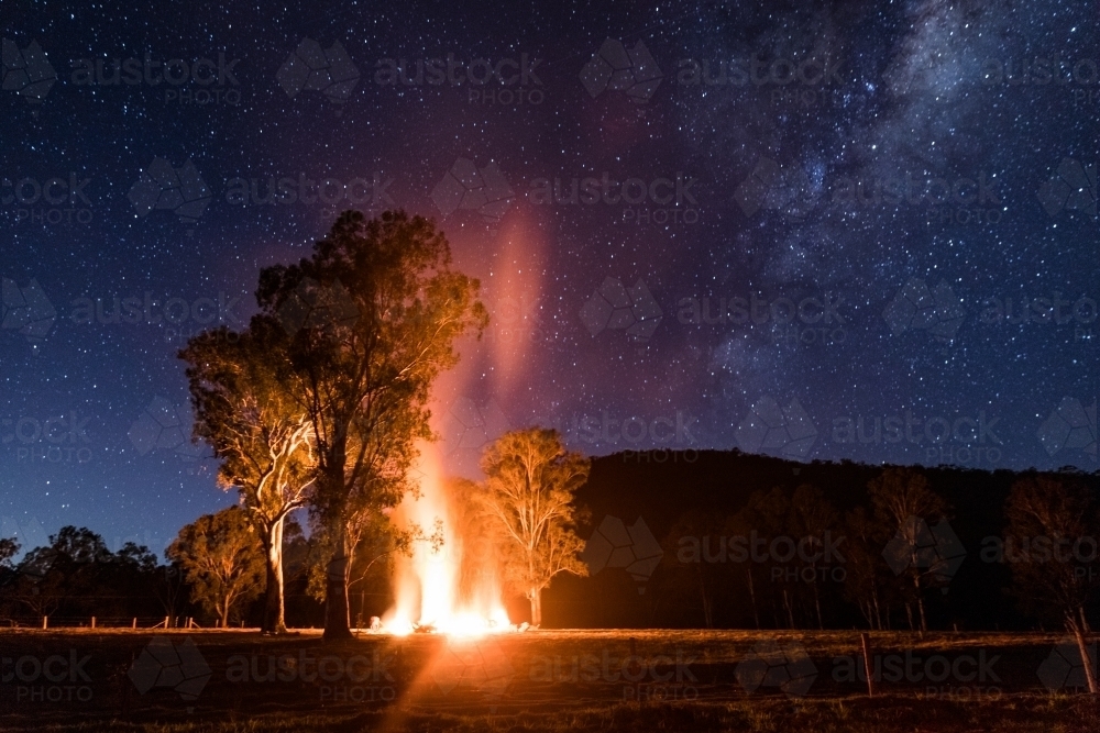 Night scene with a bonfire under some trees and the Milky Way - Australian Stock Image