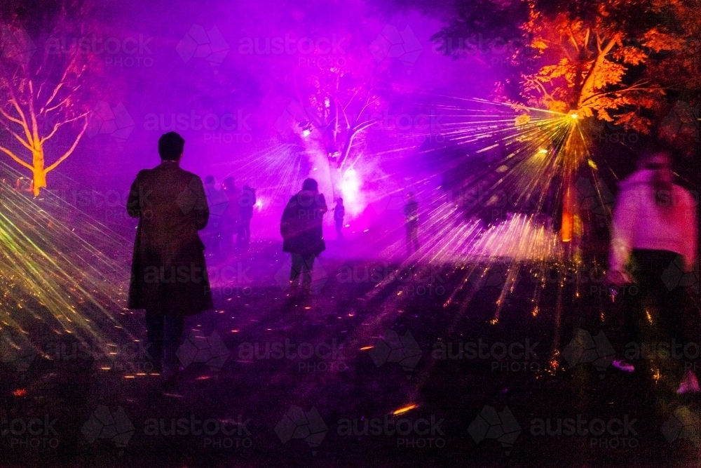 Night time laser light display with beams of colourful light shining through fog - Australian Stock Image