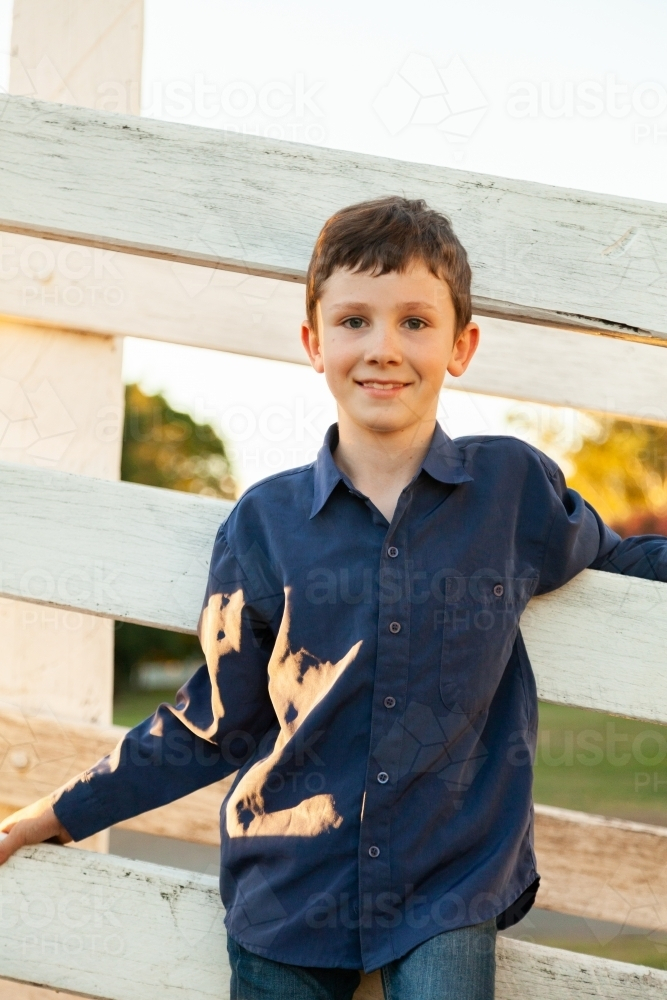 Nine year old boy leaning against white fence - Australian Stock Image