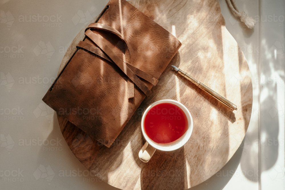 notebook sitting on a wooden board with pen and cup of tea on the side - Australian Stock Image