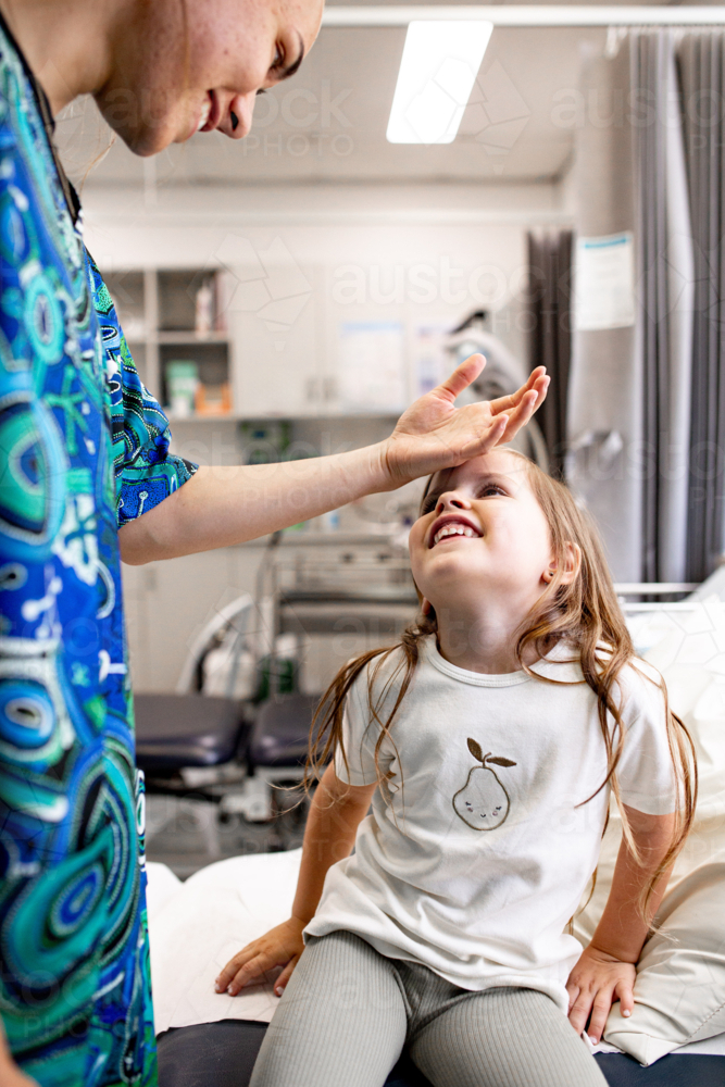 Nurse gently examining child's temperature on forehead in clinic setting - Australian Stock Image