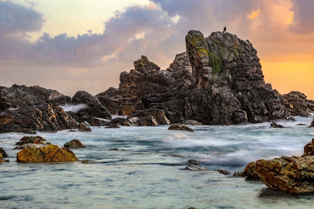 Ocean and rocky coastline against cloudy sunrise - Australian Stock Image
