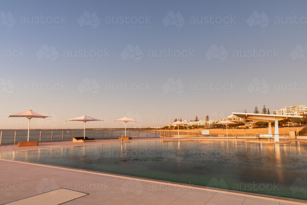 Ocean pool with 4 white umbrellas at sunrise - Australian Stock Image