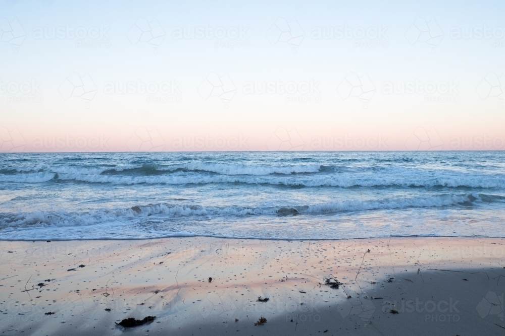 Ocean waves lapping and light reflections in the sand in the morning pastel pink light - Australian Stock Image