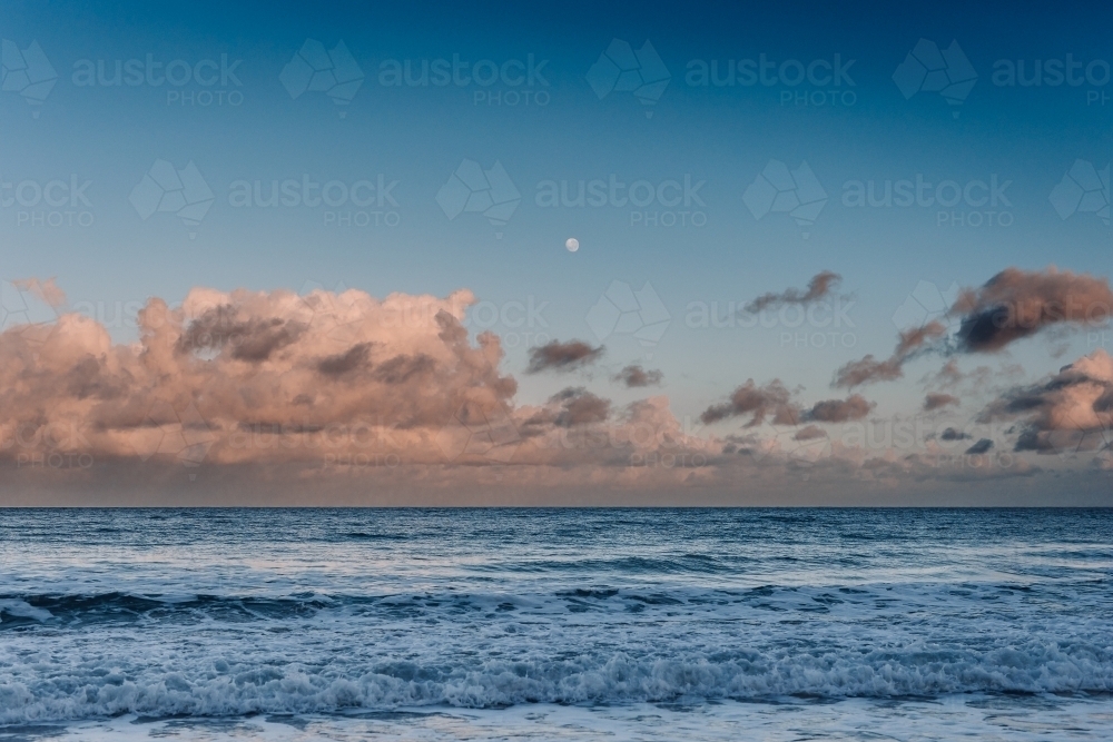Ocean with pink clouds and moon - Australian Stock Image