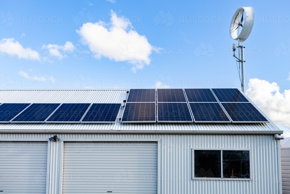 off grid sustainable living with solar panels and wind turbine on shed roof - Australian Stock Image