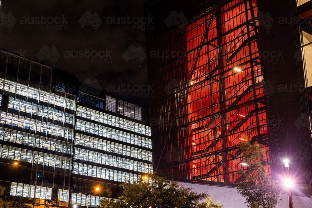 Office building at night, windows illuminated white and stairwell of other building illuminated red - Australian Stock Image