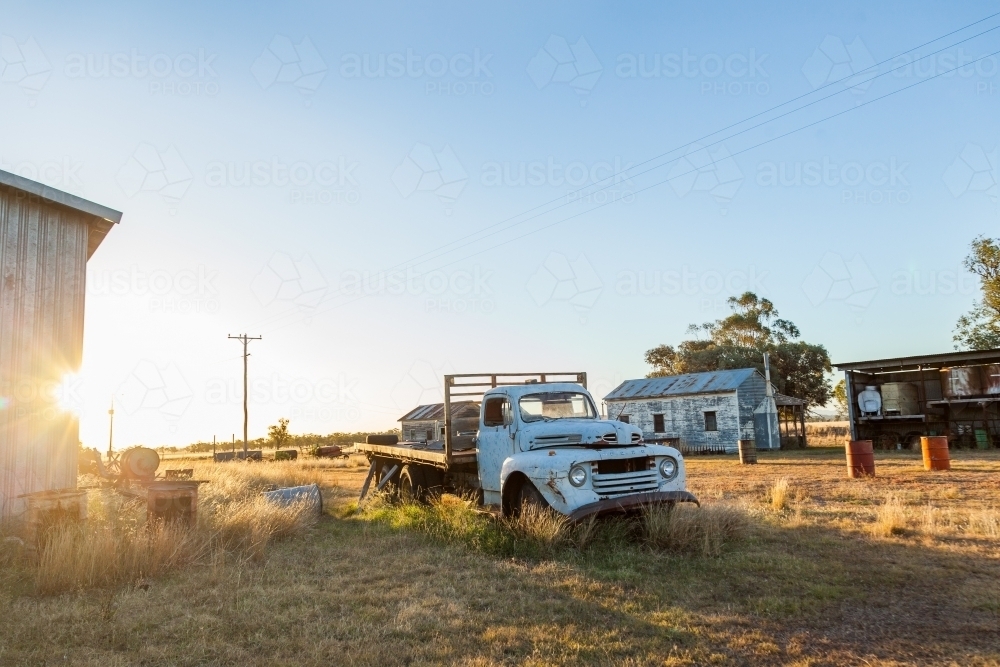 Old blue truck and other junk sitting in farm paddock at sunset - Australian Stock Image
