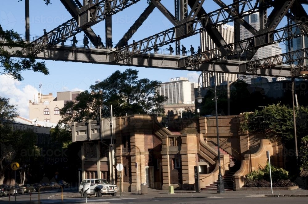 Old buildings viewed under iron girders of the Sydney Harbour Bridge with bridge climbers - Australian Stock Image