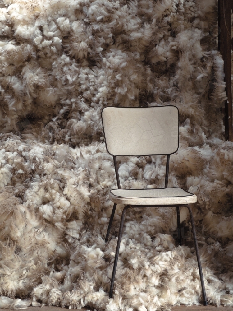 Old chair in front of wool pile at shearing time - Australian Stock Image