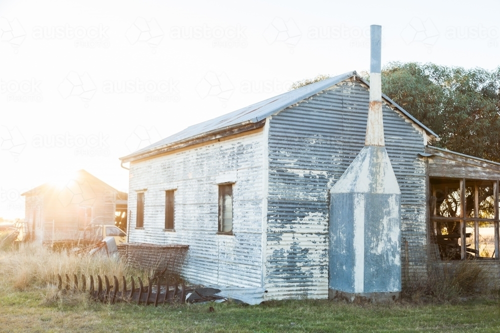 Old corrugated iron building on farm with sun flare over it - Australian Stock Image