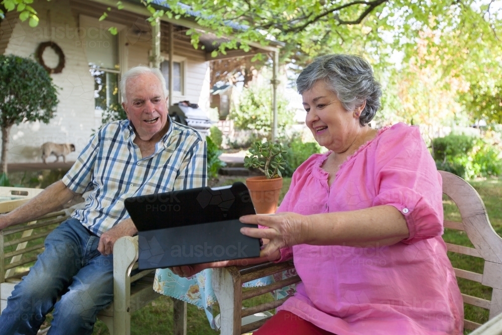 Old couple sitting on the bench looking at their tablet - Australian Stock Image