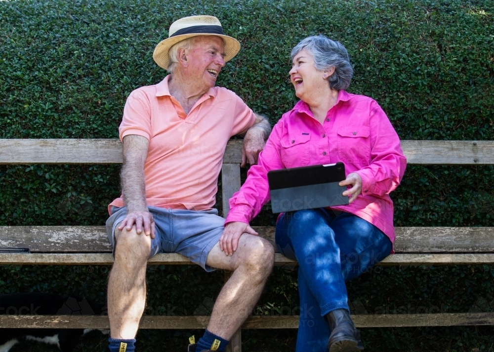Old couple sitting on the bench looking at their tablet - Australian Stock Image