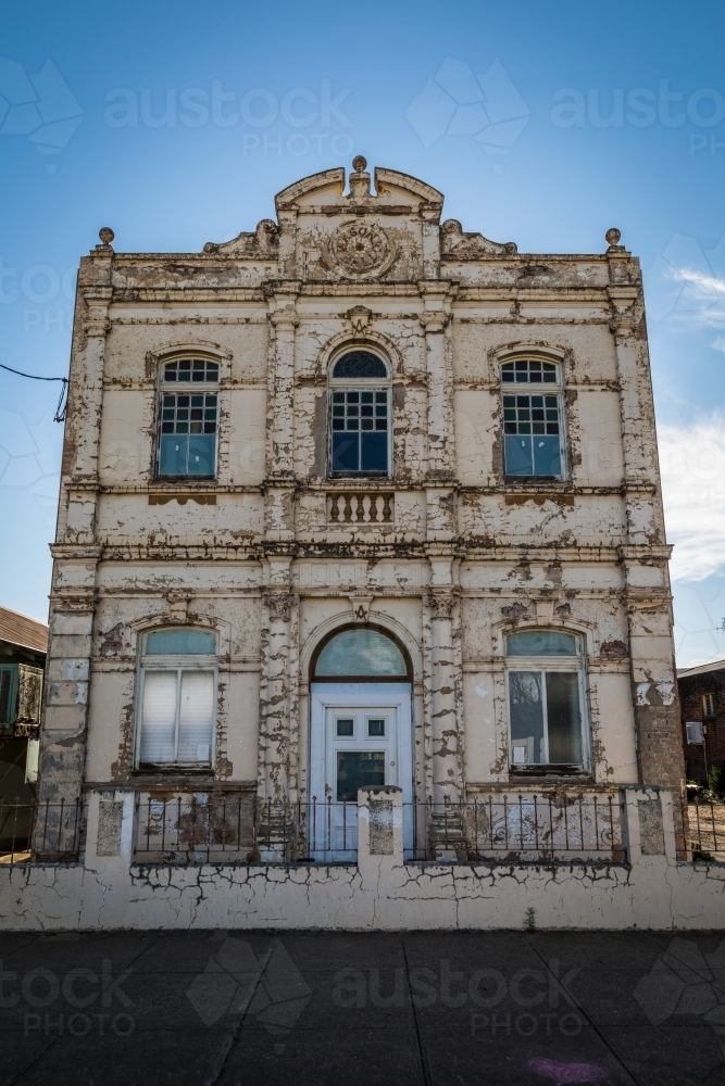 Old derelict building with weathered facade standing grand against a blue sky - Australian Stock Image