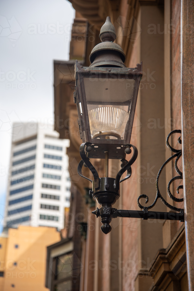 Old light on a sandstone building with modern buildings in the background - Australian Stock Image