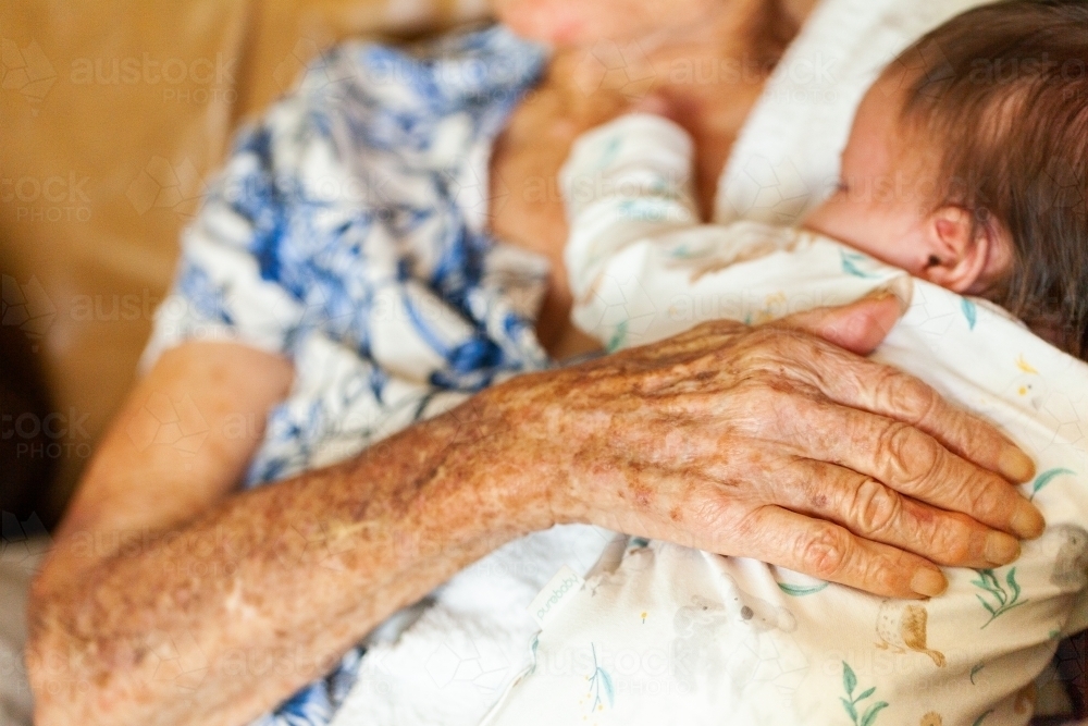 Old loving hands of great granny on sleepy newborn baby - Australian Stock Image