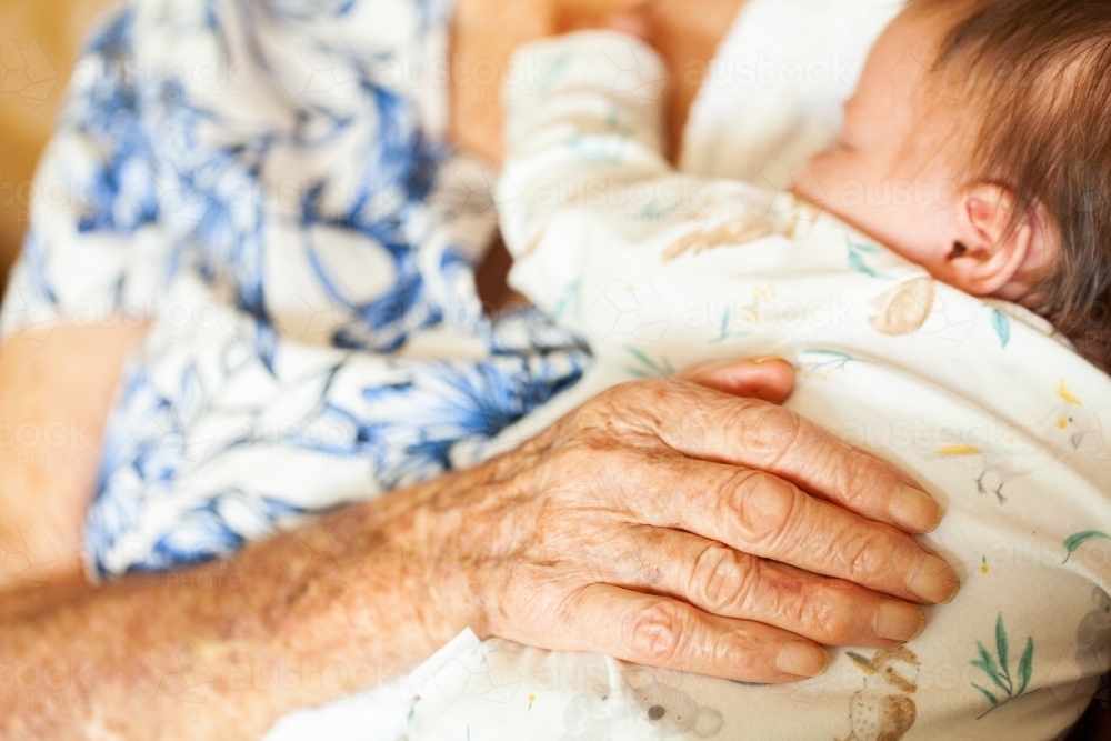 Old loving hands of great granny on sleepy newborn baby - Australian Stock Image