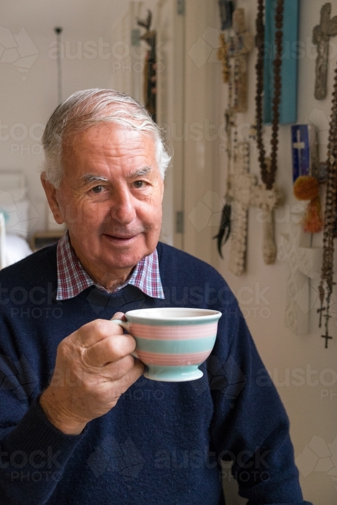 Old man with a cup of tea looks at the camera - Australian Stock Image