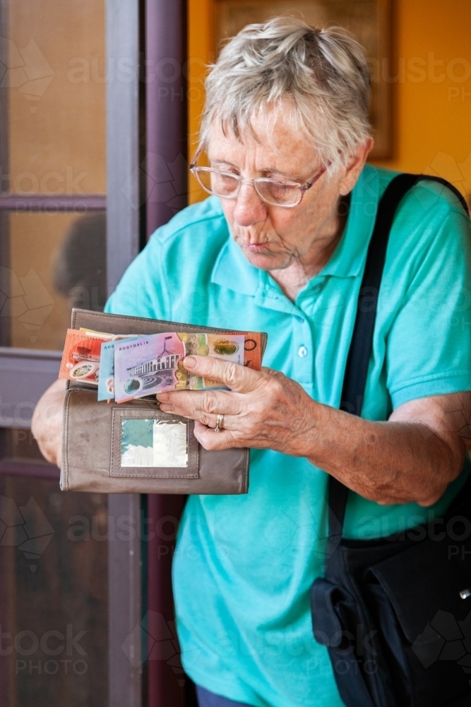 Old person at front door handing over cash from wallet - Australian Stock Image