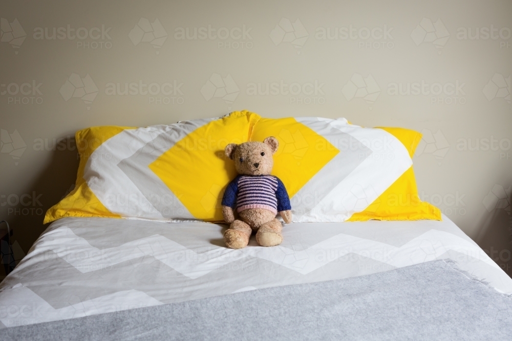 Old teddy bear alone on a double bed - Australian Stock Image