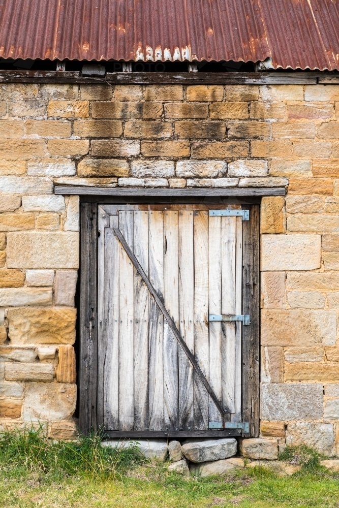 Old timber door on stone brick building with rusted corrugated roof. - Australian Stock Image
