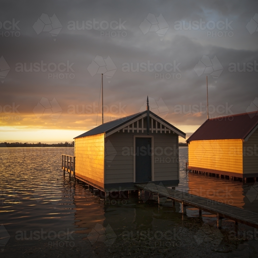 Old weathered boat sheds on lake at sunset - Australian Stock Image
