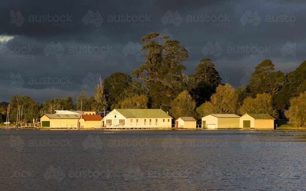 old weathered boat sheds on lake with dark sky - Australian Stock Image