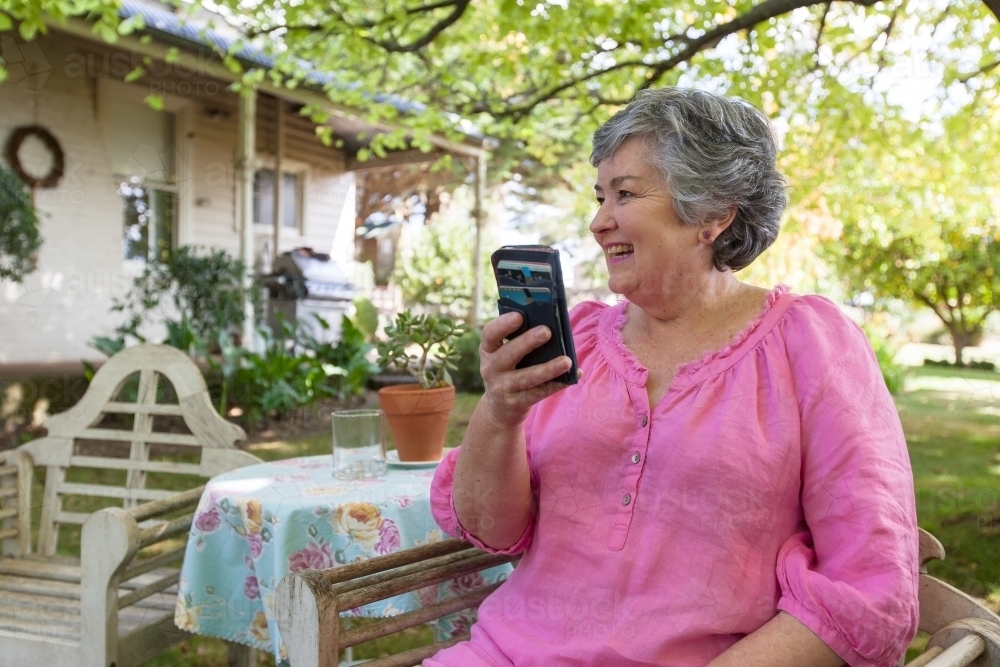 Old woman sitting in backyard looking at her mobile phone - Australian Stock Image