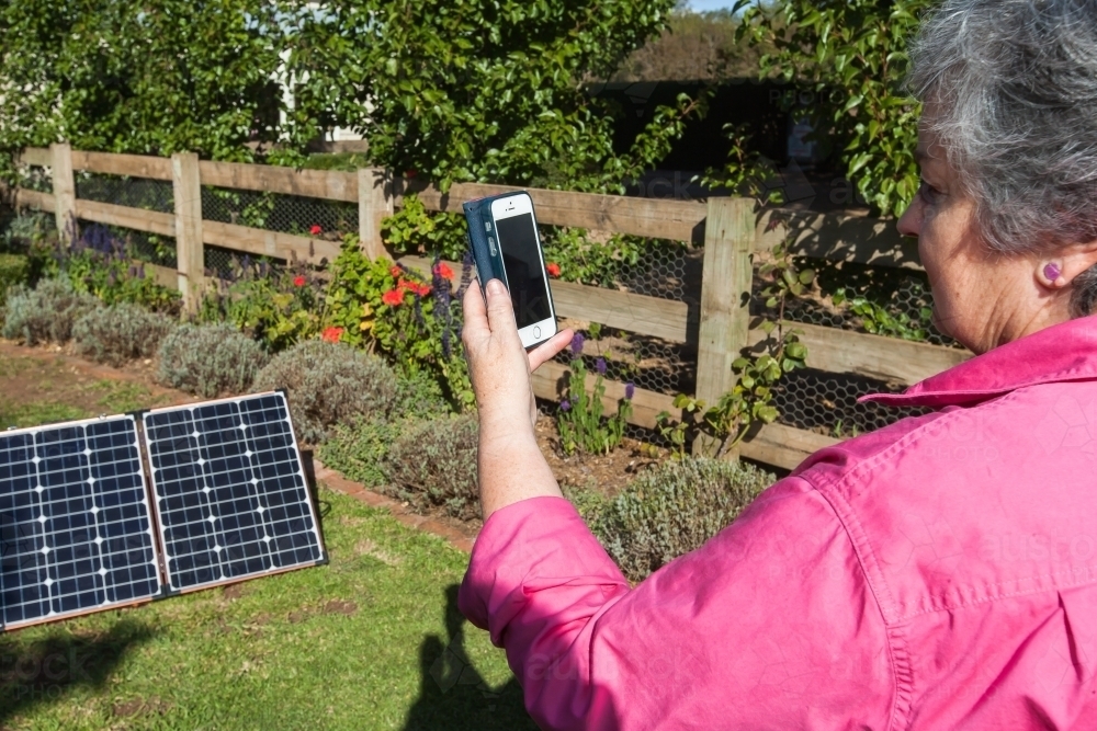 Old woman with her smartphone screen outdoors on field with solar panels - Australian Stock Image
