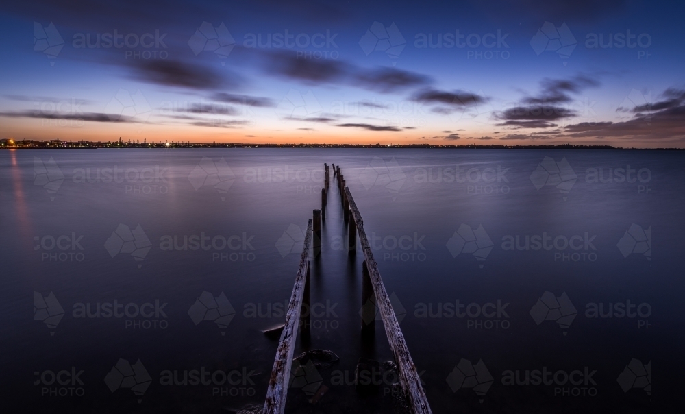 Old worn and weathered jetty leading into the sea at sunset - Australian Stock Image
