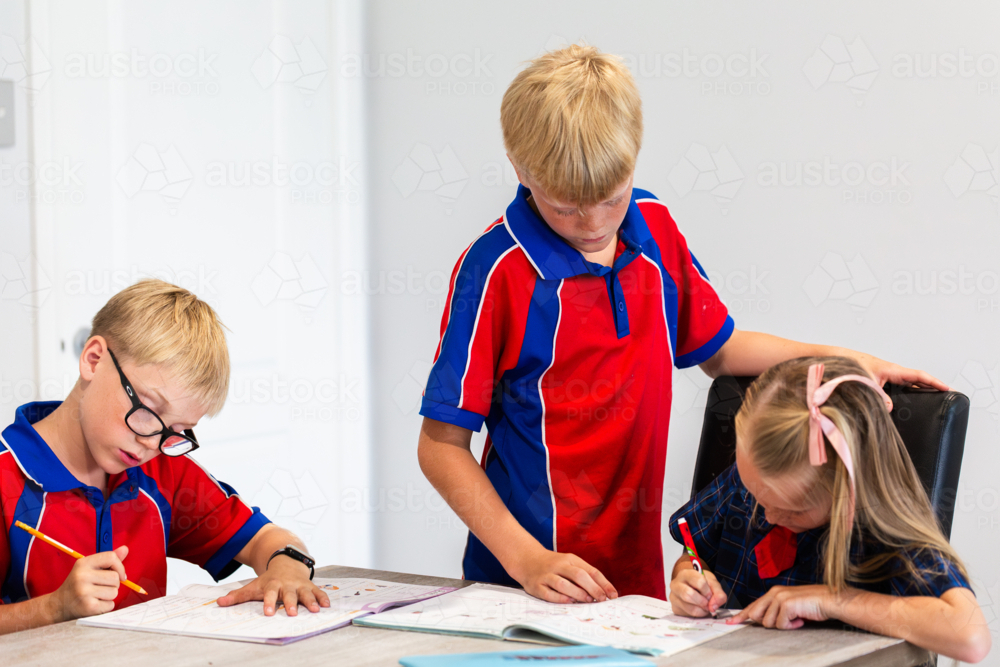 Older brother helping younger sister with her homework in workbook at table indoors - Australian Stock Image