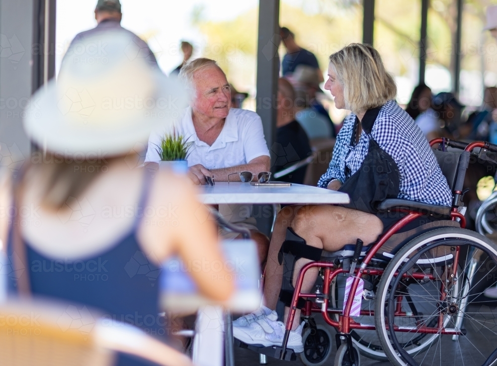 older couple in cafe with woman in wheelchair and blurred person in foreground - Australian Stock Image