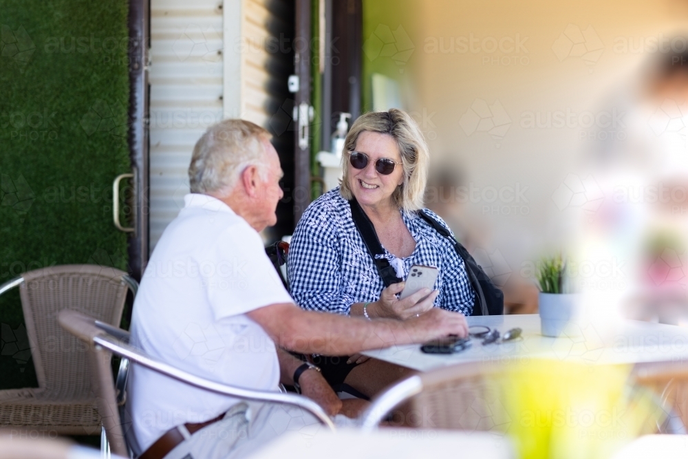 Image of older couple sitting at cafe table and she is holding a phone ...