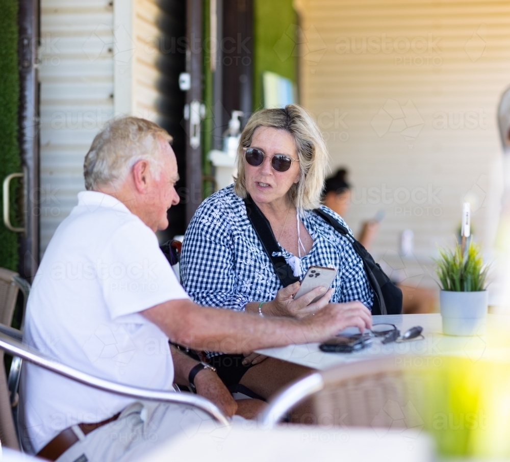 older couple sitting at cafe table engaging in conversation - Australian Stock Image