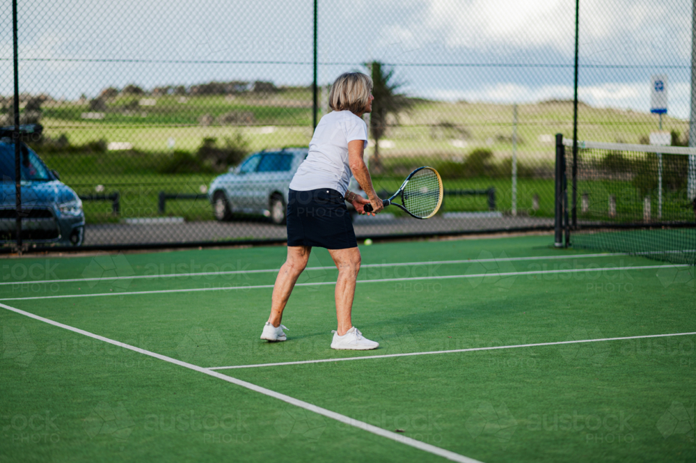 Older female athlete prepares to hit the tennis ball on green court - Australian Stock Image
