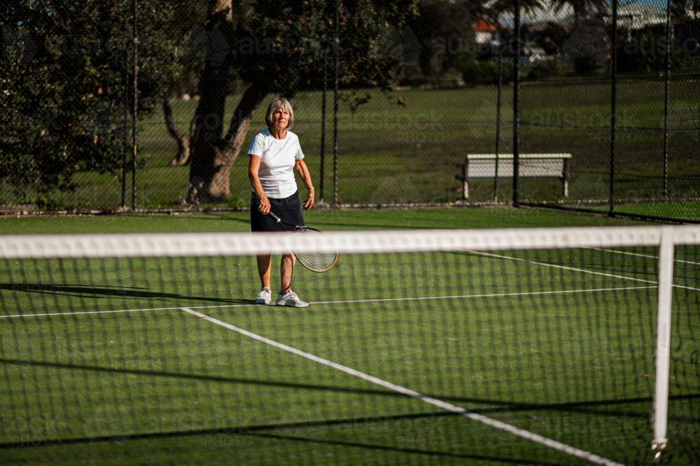 Older female athlete prepares to serve on tennis court - Australian Stock Image