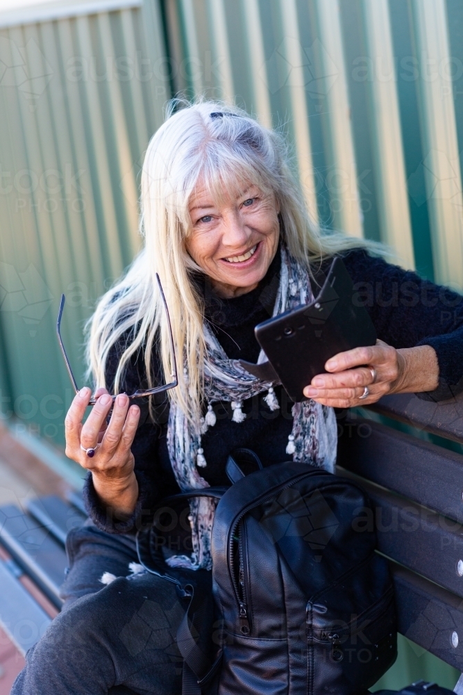 Older lady holding mobile phone and smiling - Australian Stock Image