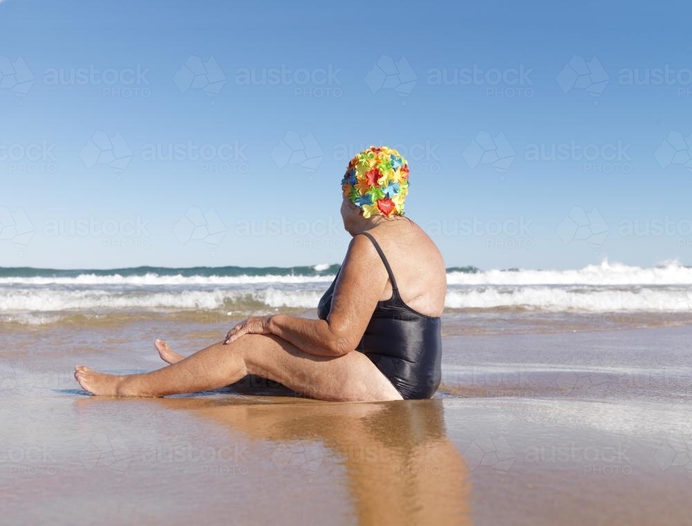 Older lady in swimmers sitting on the beach - Australian Stock Image