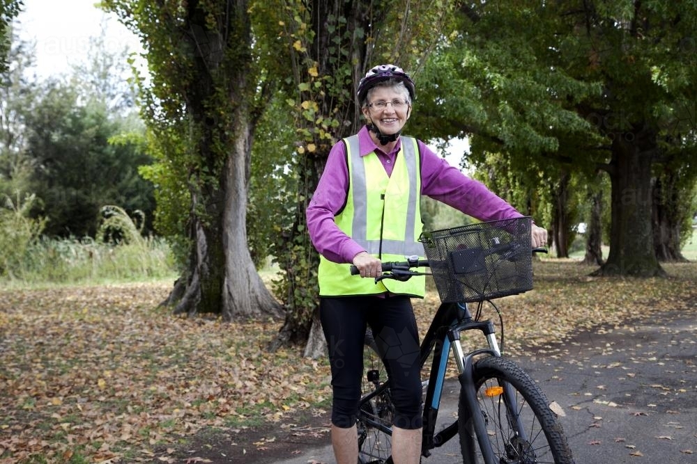 Older lady wearing high visibilty vest standing with bike - Australian Stock Image