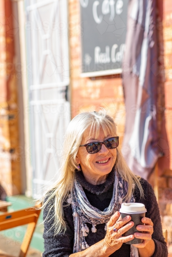 older lady wearing sunnies and holding takeaway coffee cup - Australian Stock Image