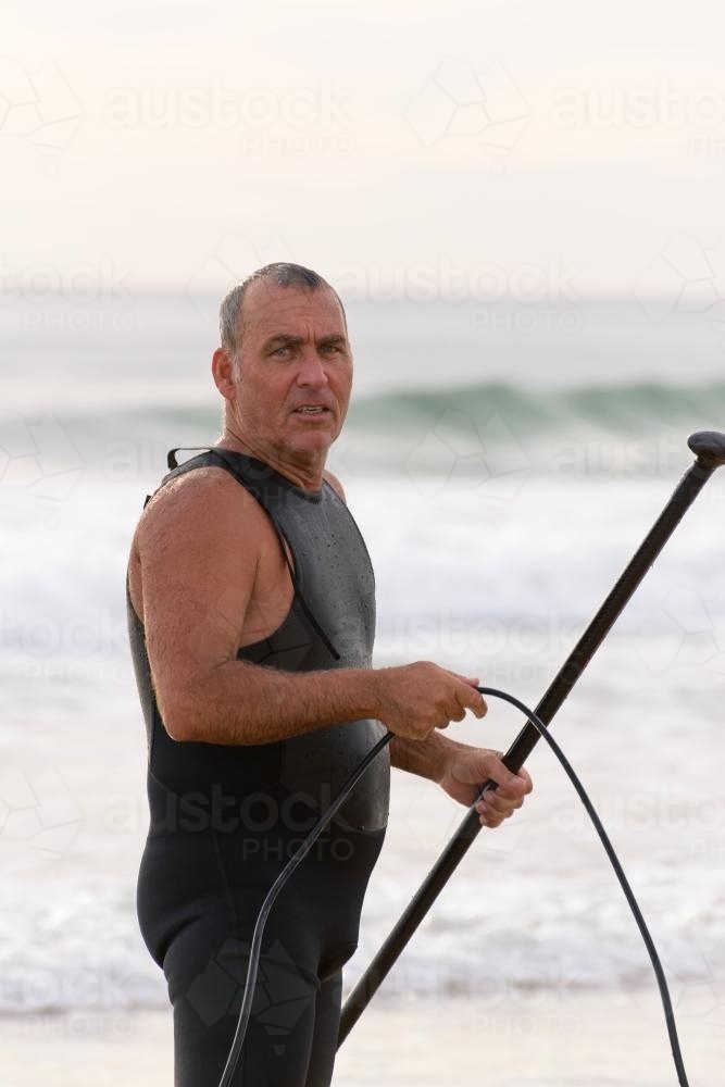 Older man at beach in wetsuit - Australian Stock Image