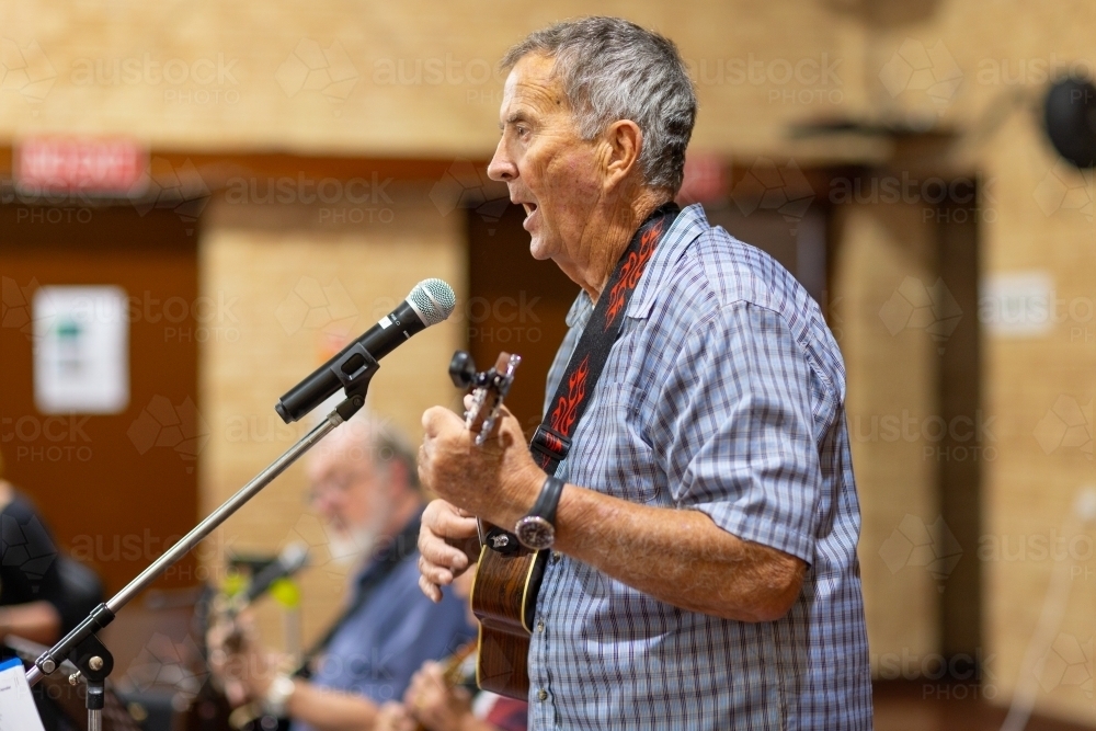 older man playing ukelele and singing into microphone - Australian Stock Image